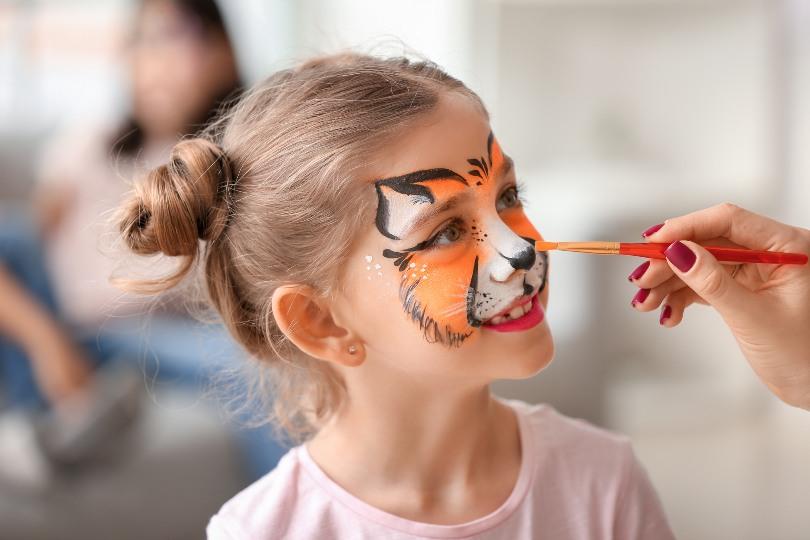 Mädchen kriegt ein Tigergesicht geschminkt - Dschungelparty zum Kindergeburtstag